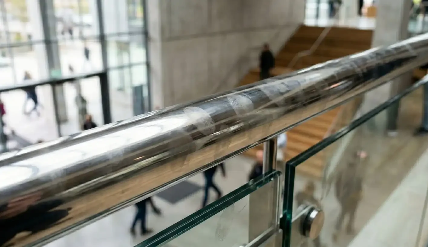 Close-up of a mirror polished stainless steel balustrade handrail with glass infill showing fingerprints on the reflective surface
