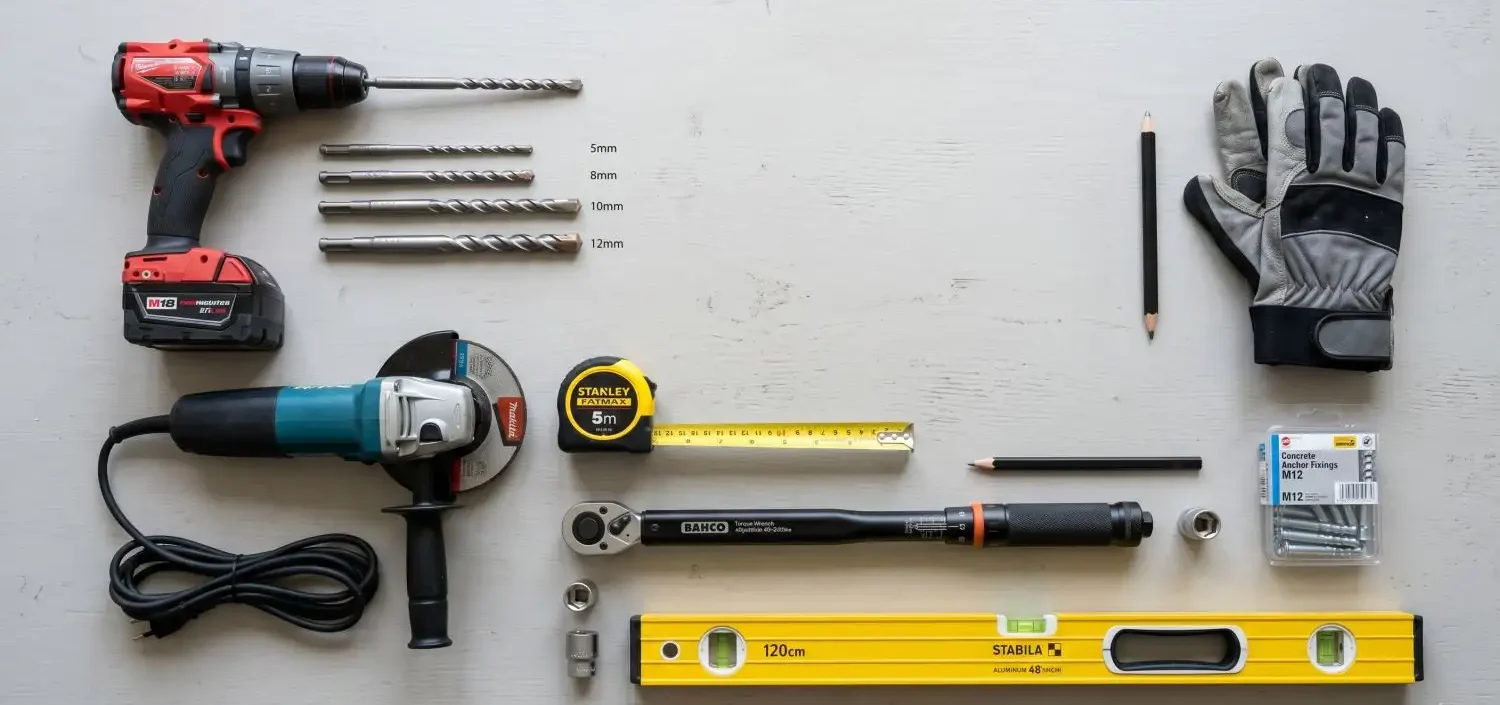 Flatlay of tools needed for a DIY balustrade installation including a drill, drill bits, angle grinder, tape measure, torque wrench, spirit level, gloves, and concrete anchor fixings